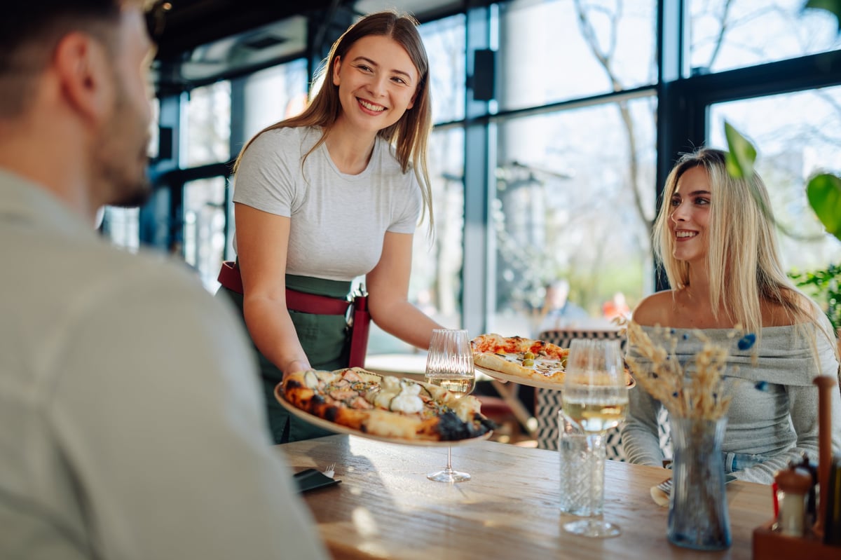 Smiling waitress serving freshly baked pizzas to guests at a party
